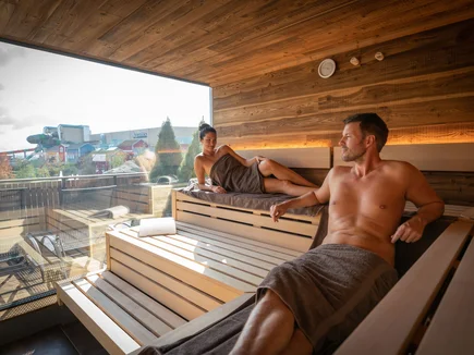 A couple sits in a panoramic sauna at hotel 'Krønasår' with a view of Rulantica water world.