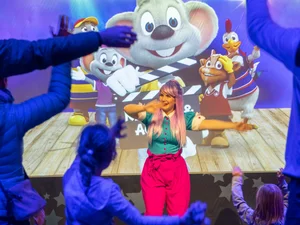 In the colourful JUNIOR CLUB studios, children dance with an entertainer in front of a screen featuring the Europa-Park mascots.