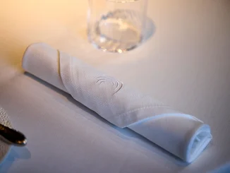A close-up of a cloth napkin from the Ammolite – House of Light restaurant at the ‘Bell Rock’ themed hotel. The white napkin lies neatly rolled on a laid table.