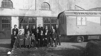The Mack family stand in front of the wagon factory building, with circus wagons in the background.