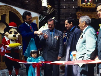 Roland, Franz und Jürgen Mack schneiden gemeinsam mit der Euromaus und Gästen ein rot-weißes Band zur Eröffnung des Schweizer Themenbereichs im Europa-Park durch.