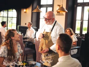 A sommelier pours wine and advises restaurant guests at Amitié – La Cuisine du Château.