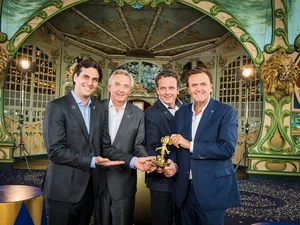 Thomas Mack, Jürgen Mack, Michael Mack and Roland Mack hold a small golden trophy in their hands that looks like a mouse.