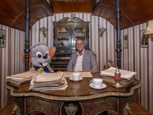 Roland Mack sits at a desk in a historic circus wagon with a large Ed soft toy.