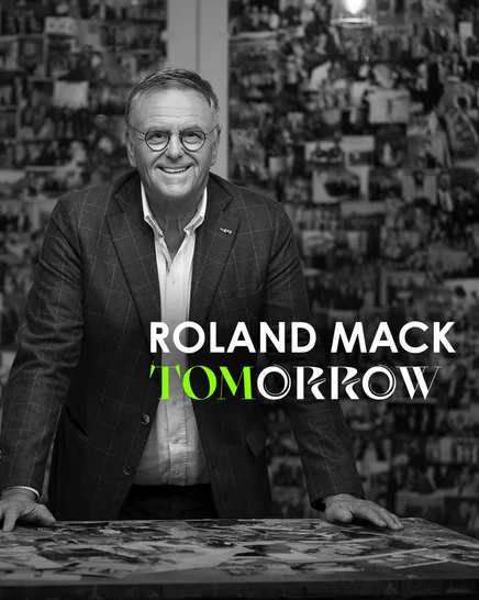 Roland Mack im TOMorrow Podcast Schwarz-weiß Aufnahme von Roland Mack vor einer Wand voller Fotos.