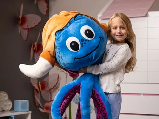 Girl holding a giant plush Snorri in her arms.