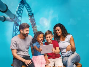 A family is looking at content on a tablet. A rollercoaster can be seen in the background.