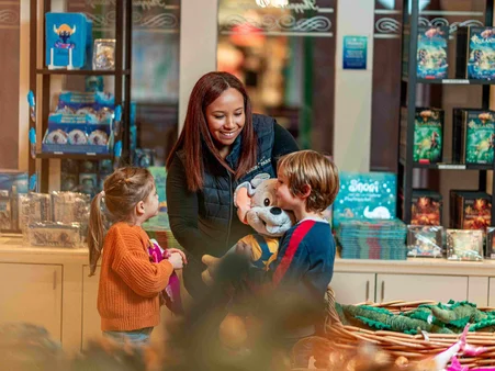 An employee in a merchandise shop at Europa-Park presents an Ed Euromaus soft toy to two delighted children.