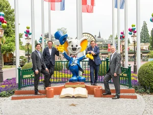 Thomas Mack, Michael Mack, Jürgen Mack and Roland Mack stand around a huge Euromaus sculpture in front of the main entrance to Europa-Park.