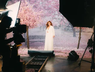 Des caméras et des spots sont dirigées vers Andrea Berg, au centre. Derrière elle, on voit un arrière-plan onirique empli de cerisiers en fleurs.