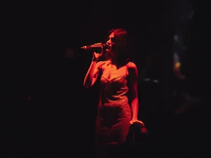A woman sings in the dark, illuminated only by a lamp.