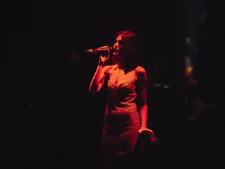 Exclusive performances just for you A woman sings in the dark, illuminated only by a lamp.