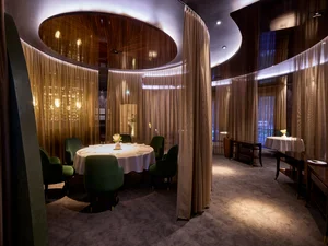 The elegant interior of the two-star Michelin restaurant Ammolite – House of Light at the Europa-Park Resort. High-quality seating areas separated by curtains.