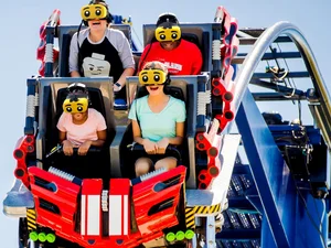 Passengers on The Great LEGO® Race attraction at LEGOLAND Florida, equipped with yellow VR headsets with oversized eyes.