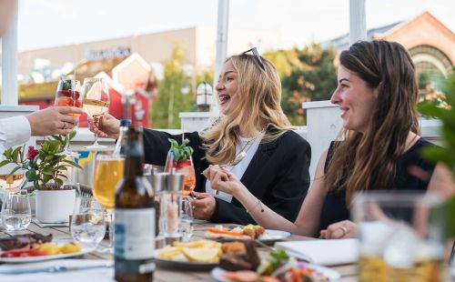 Zwei fröhliche Frauen sitzen draußen beim Dinner in einem Restaurant des Europa-Park.