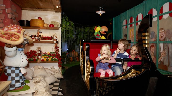 Kinder sitzen in der Attraktion Piccolo Mondo im Italienischen Themenbereich des Europa-Park. Sie fahren an einer Figur eines Pizzabäckers vorbei.