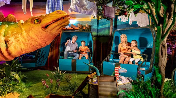 Des visiteurs à bord des nacelles à travers le jardin des dinosaures dans l’attraction Madame Freudenreich Curiosités.