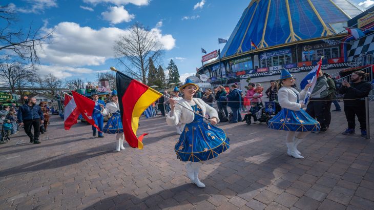 Des danseuses agitent divers drapeaux nationaux pendant une parade à Europa-Park. De nombreux visiteurs se tiennent en arrière-plan.