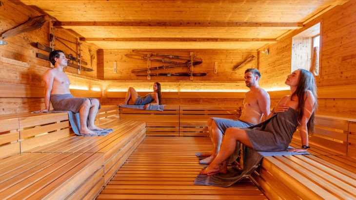Plusieurs personnes se détendent avec des masques faciaux dans le sauna « lille » dans l’espace détente et sauna exclusif Hyggedal à Rulantica.