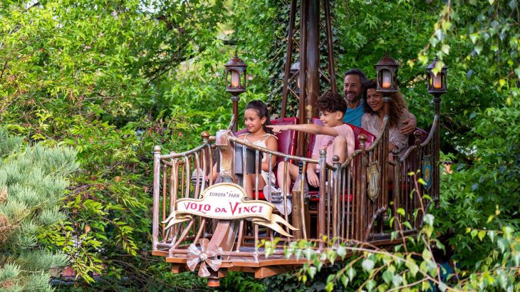 Eine Familie mit zwei Kindern in der Attraktion Volo da Vinci im Europa-Park. Ein Kind zeigt begeistert in die Ferne.