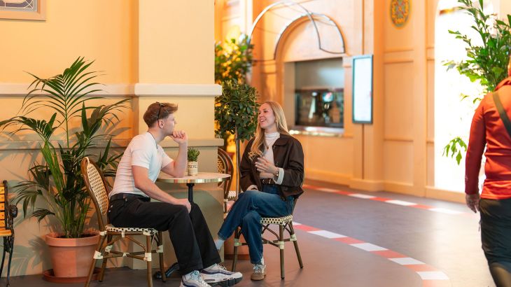 Una coppia è seduta a un tavolo nell’area interna del quartiere tematico monegasco dell’Europa-Park. Sullo sfondo si riconosce il Café de Paris.