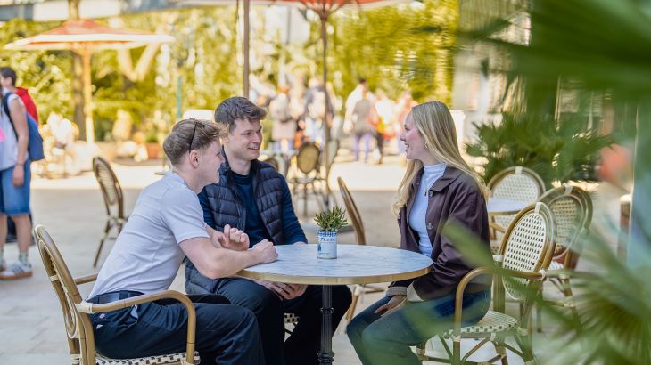 Drei Personen sitzen an einem Tisch im Außenbereich des Monegassischen Themenbereichs im Europa-Park.
