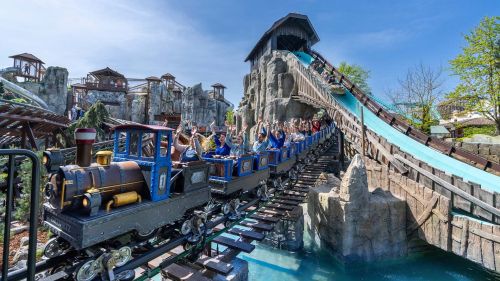 Ein Zug der Familienachterbahn Alpenexpress "Enzian" fährt unter der Wasserattraktion Tiroler Wildwasserbahn durch.