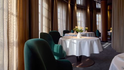 Vue intérieure du restaurant « Ammolite – House of Light » à l’hôtel thématique « Bell Rock ». Le tables sont dressées avec un vase blanc et des fleurs sur chacune. L’atmosphère est moderne et noble.