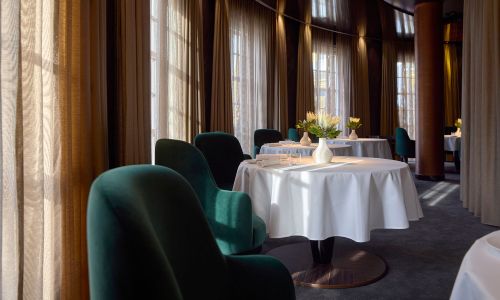Vue intérieure du restaurant « Ammolite – House of Light » à l’hôtel thématique « Bell Rock ». Le tables sont dressées avec un vase blanc et des fleurs sur chacune. L’atmosphère est moderne et noble.